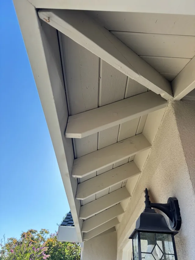 Underside of painted eaves and rafter tails against a blue sky
