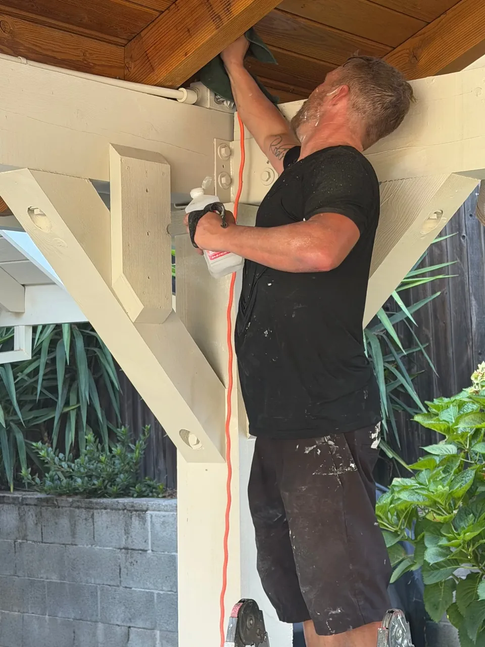 A painter working overhead on the underside of a pergola